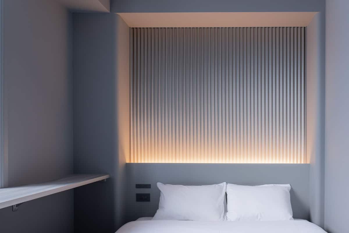 Ein modernes Schlafzimmer mit einem Bett, weißen Kissen und einer vertikalen Leuchtpaneele.
