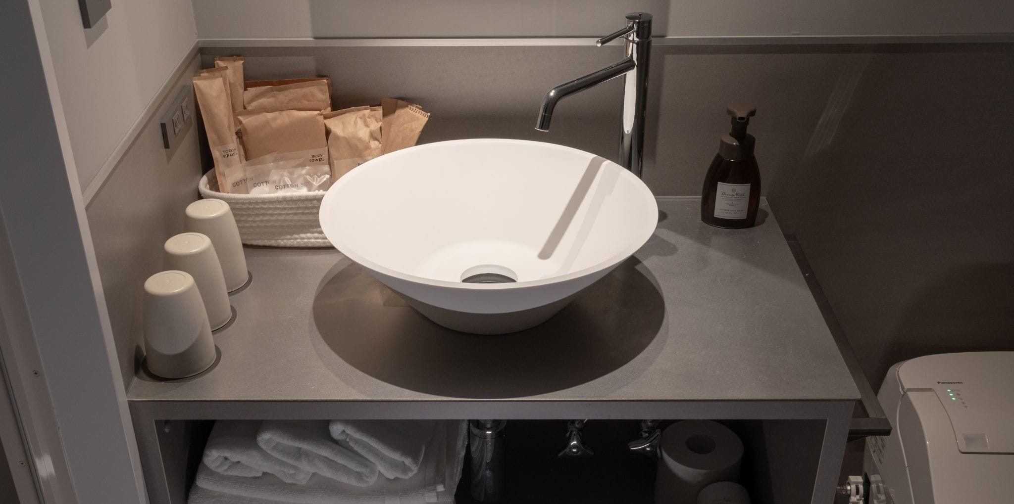 A bathroom with a white vessel sink, a toilet paper holder, and a bottle of hand soap.