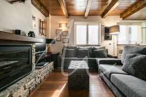 A cozy living room with a stone fireplace, a large flat-screen TV, a sofa, and a coffee table. - Forcanada (Vielha e Mijaran)