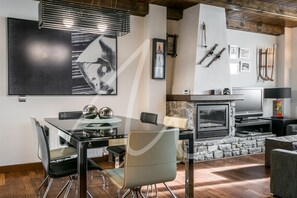 A modern living room with a stone fireplace, a dining area with a glass table, and a TV mounted on the wall. - Forcanada (Vielha e Mijaran)