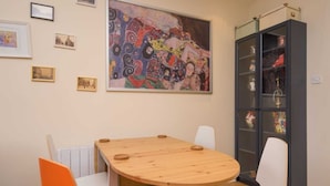 A dining area with a round wooden table, white chairs, and a colorful abstract painting above.