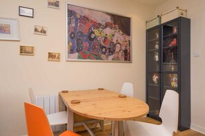 A dining area with a round wooden table, white chairs, and a colorful abstract painting above. - Leeds City Centre 
Stylish Apartment Superb Location, sleeps up to 6 (Leeds)