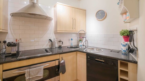 A modern kitchen with a stove, oven, sink, and a clock on the wall.