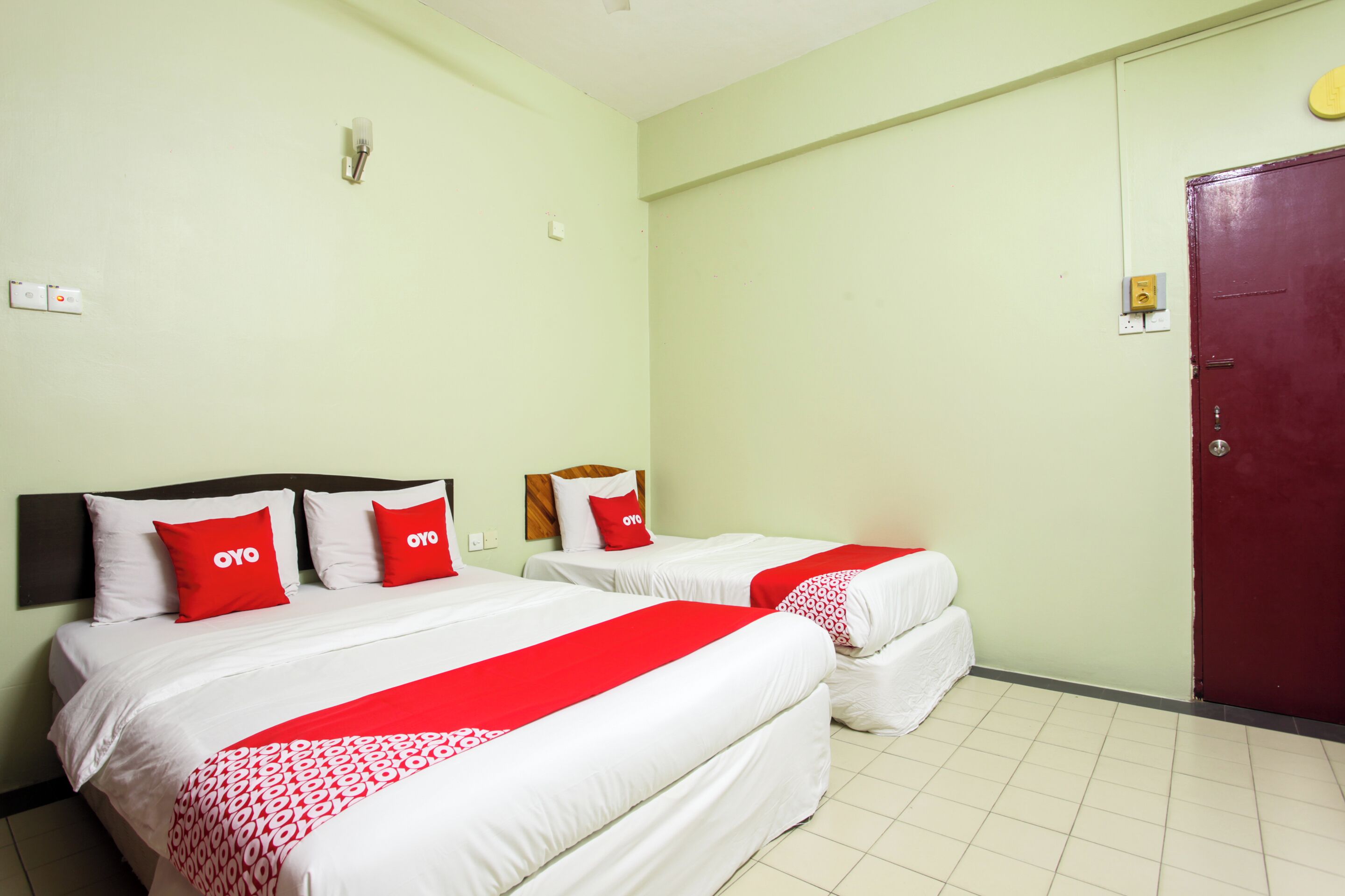 A hotel room with two beds, each with white bedding and red accents, a red door, and a light green wall.