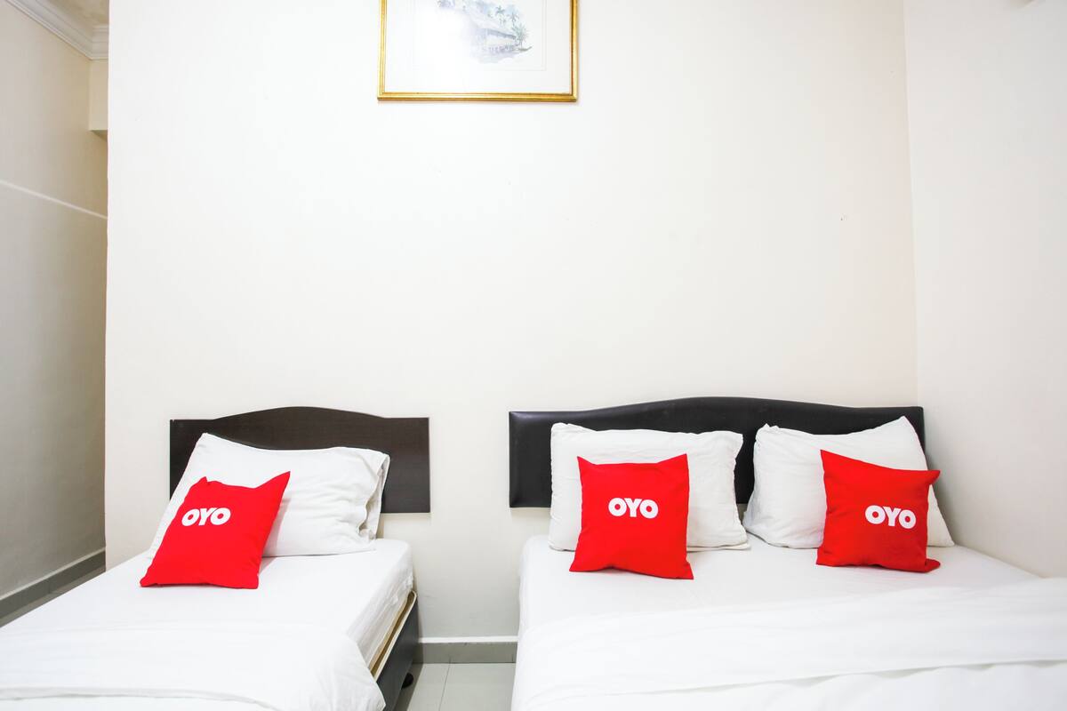 Une chambre d’hôtel avec deux lits, chacun étant équipé de draps blancs et d’oreillers rouges portant le logo « OYO ».