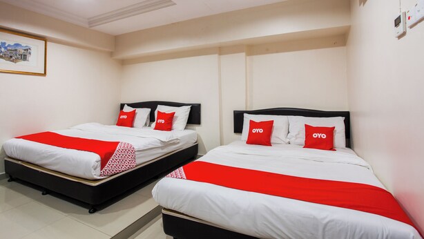 A hotel room with two beds, each with white bedding and red accents, a framed picture on the wall, and an air conditioning unit. - OYO 89549 Casavilla Hotel (city Centre) Taiping (Taiping)