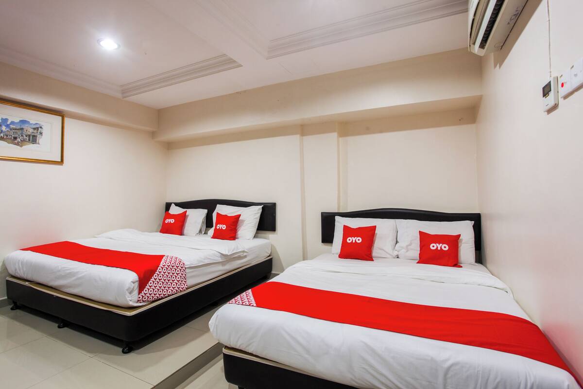 Une chambre d’hôtel avec deux lits, chacun agrémenté de draps blancs et de touches de couleur rouge, un tableau encadré au mur et un appareil de climatisation.