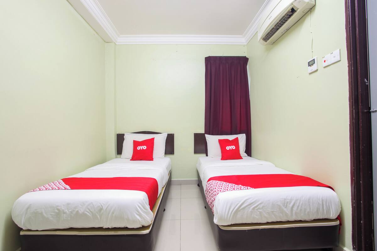 Une chambre avec deux lits, chacun agrémenté de draps blancs et de touches de couleur rouge, un rideau rouge et un appareil de climatisation fixé au mur.