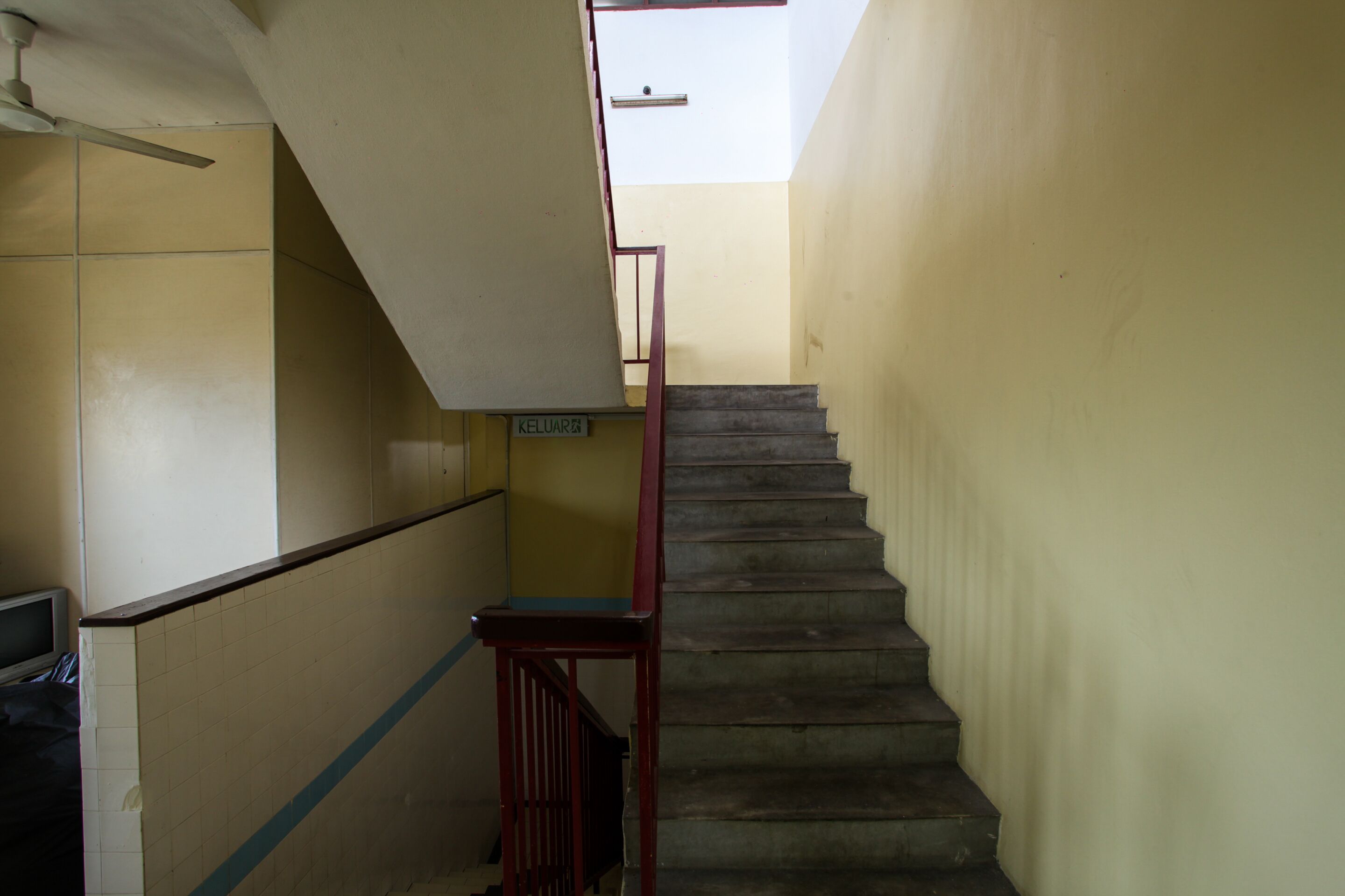 Eine enge Treppe mit rotem Geländer und einem Schild mit der Aufschrift 'KELUAR'.