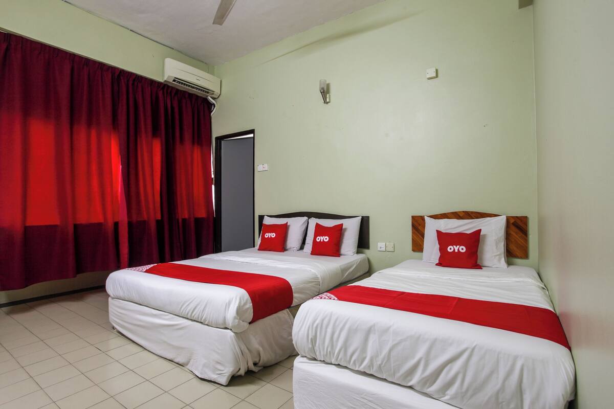 Une chambre d’hôtel avec deux lits, une literie rouge et blanche, un rideau rouge et une porte.