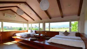 Une chambre spacieuse avec un grand lit, un lit plus petit et un coin salon offrant une vue sur l’extérieur.