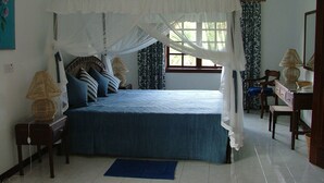 Un dormitorio con cama con dosel, una mesita de noche con lámpara, una silla y un aparador.