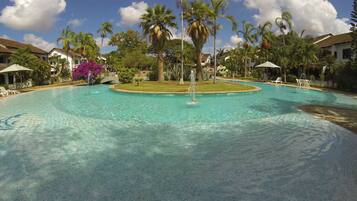 A large swimming pool with a fountain, surrounded by palm trees and lounge chairs.