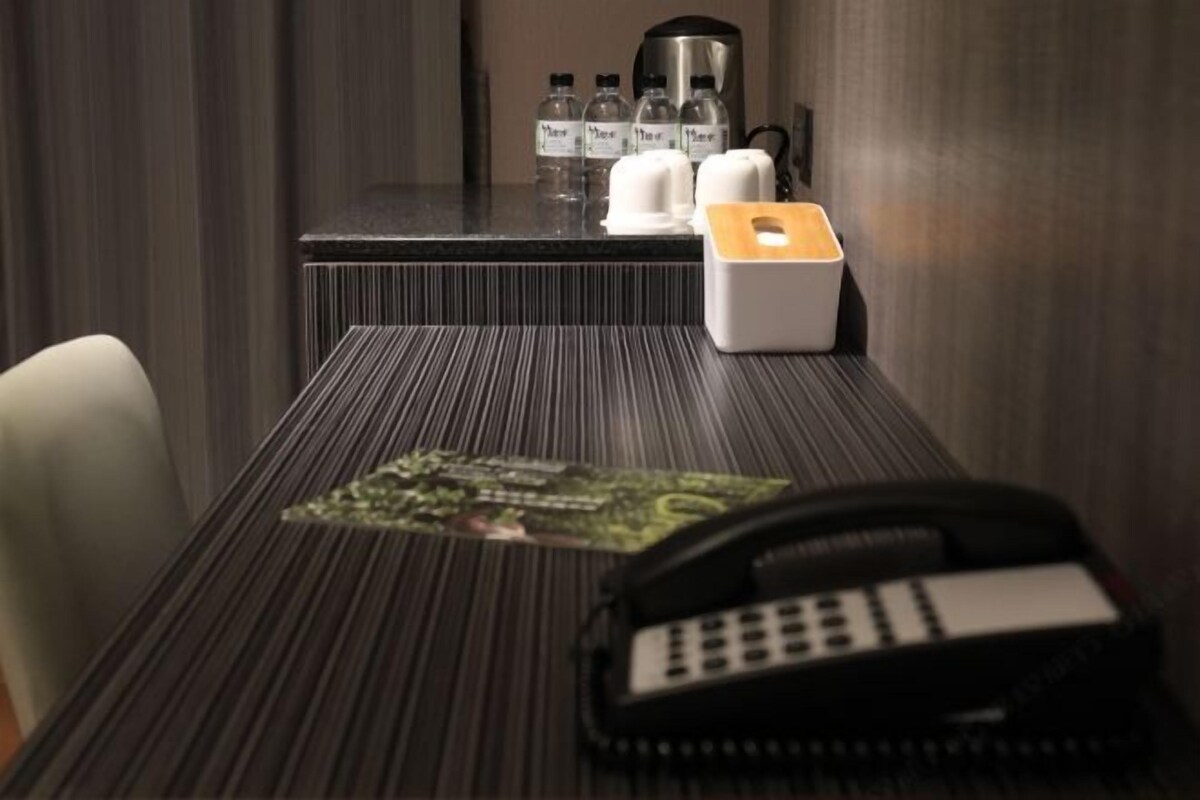 Habitación de hotel con pared a rayas, un teléfono, una cafetera y una pequeña mesa con mantel individual.