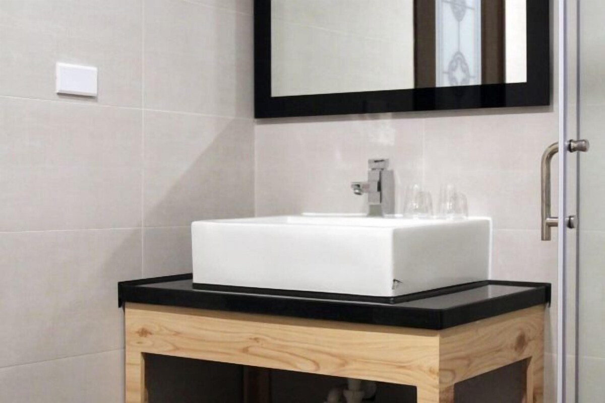 Un baño moderno con un lavabo blanco, encimera negra y mueble de madera.