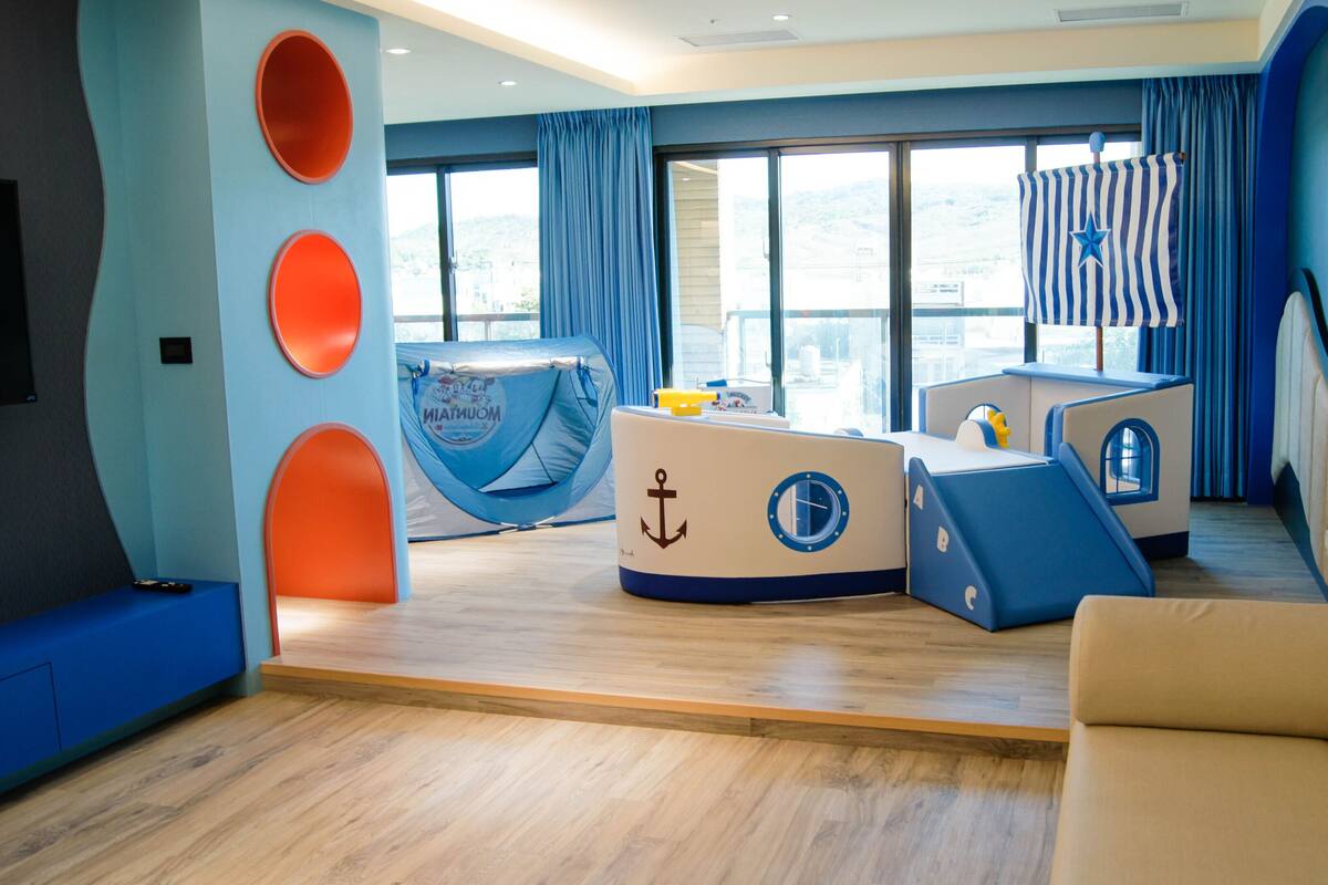 A nautical-themed room with a bunk bed, a play area, and a large window with curtains.