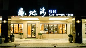Das äußere Erscheinungsbild des Hotels KueiTiWan mit gut beleuchtetem Eingang, großen Fenstern und Pflanzen in Töpfen vor dem Eingang.