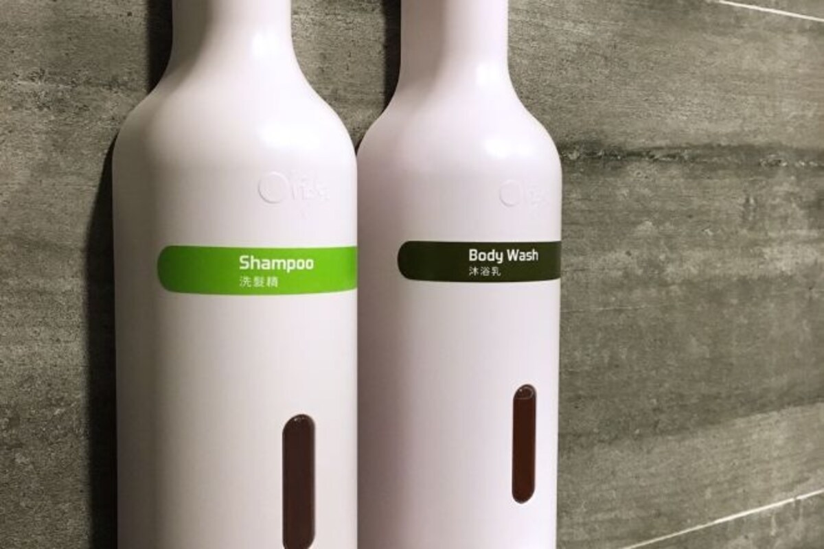 Dos botellas de productos Olay, una etiquetada como 'Shampoo' y la otra como 'Body Wash', sobre un fondo de pared con textura.