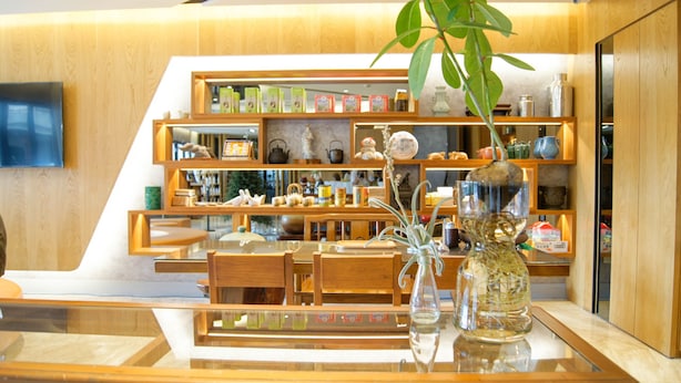 Ein modernes Interieur mit Holzmöbeln, einem Glastisch und Regalen mit verschiedenen Gegenständen.