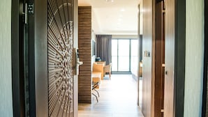 Ein moderner Hotelgang mit Holzboden, einem Essbereich mit Tisch und Stühlen sowie einem großen Fenster mit Vorhängen.