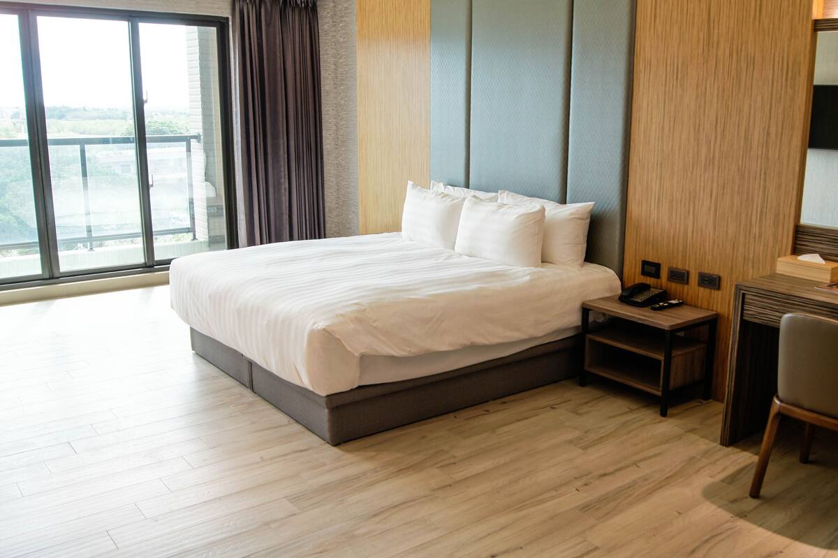 A hotel room with a large bed, a desk with a chair, a telephone, and a television.