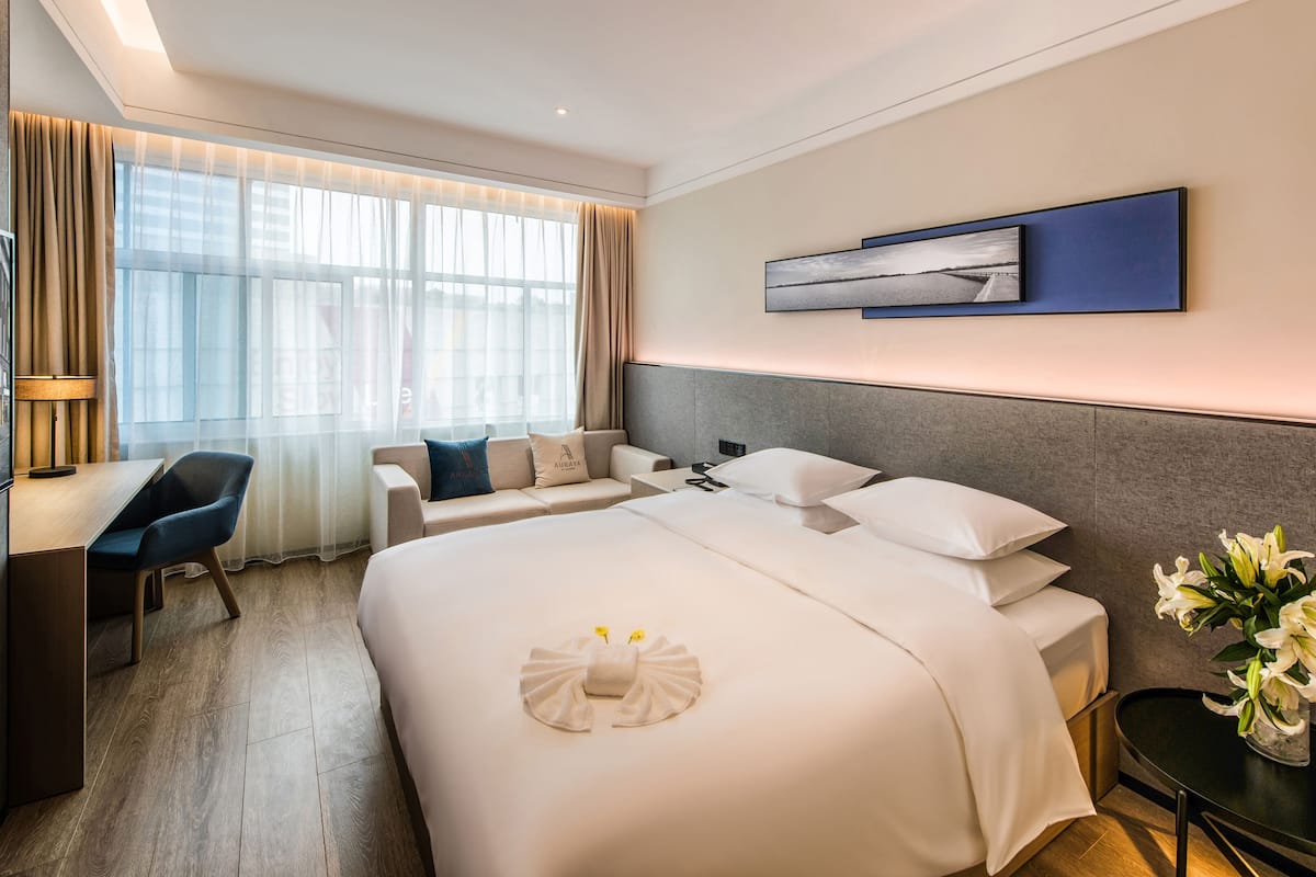 Une chambre d’hôtel avec un lit, un bureau, une chaise, une table de chevet, un vase avec des fleurs et un tableau au mur.