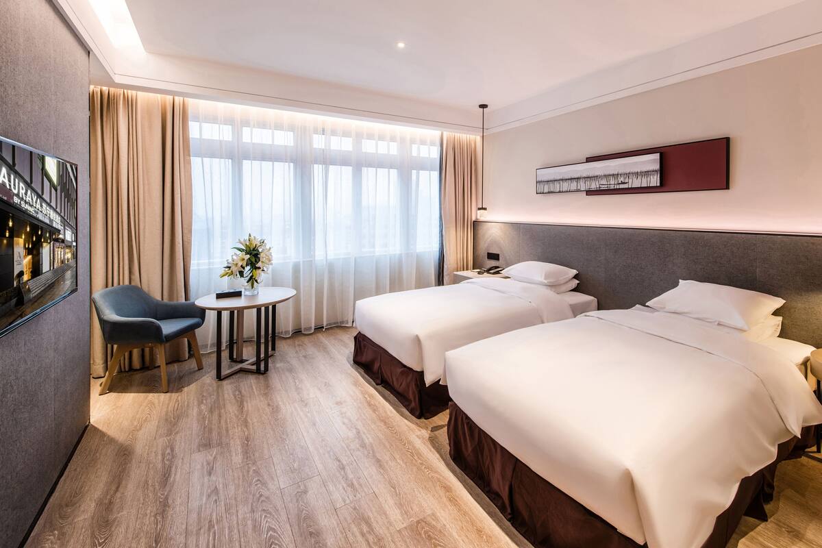 Une chambre d’hôtel avec deux lits, un bureau avec une chaise, une télévision et une lampe.