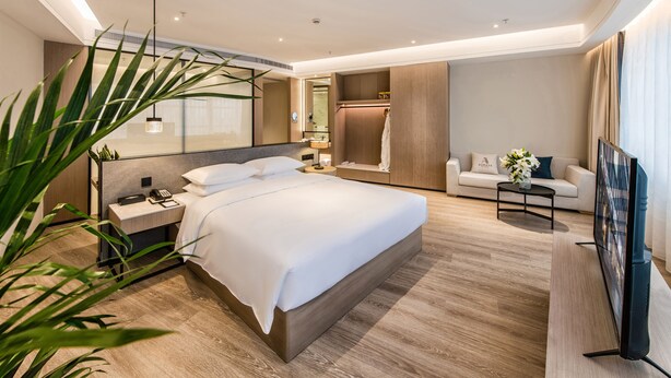 A modern hotel room with a large bed, bedside tables, a TV, a sofa, and a mirror. - Zhangjiagang Suning Auraya Hotel (Suzhou)