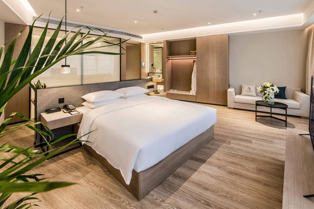 Une chambre d’hôtel moderne avec un grand lit, des tables de chevet, une télévision, un canapé et un miroir.
