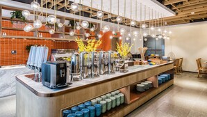 A modern cafe with a central counter, coffee machines, and a variety of bowls and plates for serving. - Zhangjiagang Suning Auraya Hotel (Suzhou)