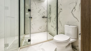 Un baño moderno con cabina de ducha de vidrio, inodoro blanco y paredes con estampado de mármol.