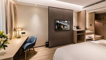 A hotel room with a bed, a desk with a chair, a TV mounted on the wall, and a wardrobe.