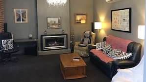 A living room with a fireplace, a chandelier, a sofa, a coffee table, and a wall-mounted air conditioner. - Top floor 3 bed apartment in the iconic Tiger Tea Building ( FREE Netflix) (Dunedin)