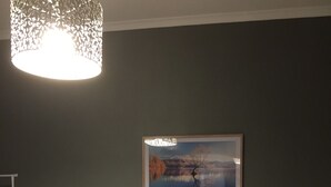 A neatly made bed with white linens, two bedside lamps, a framed landscape painting, and a digital clock on the nightstand. - Top floor 3 bed apartment in the iconic Tiger Tea Building ( FREE Netflix) (Dunedin)