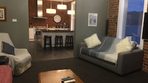 A living room with a sofa, a coffee table, and a kitchen in the background. - Top floor 3 bed apartment in the iconic Tiger Tea Building ( FREE Netflix) (Dunedin)