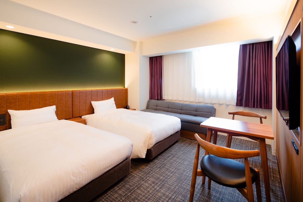 A hotel room with two beds, a sofa, a desk, and a TV.