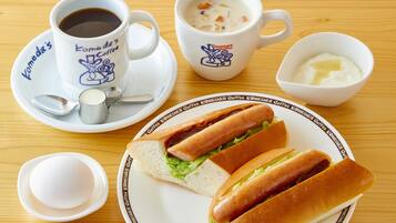 A table with a plate of hot dogs, a cup of coffee, a bowl of soup, and a small bowl of butter.