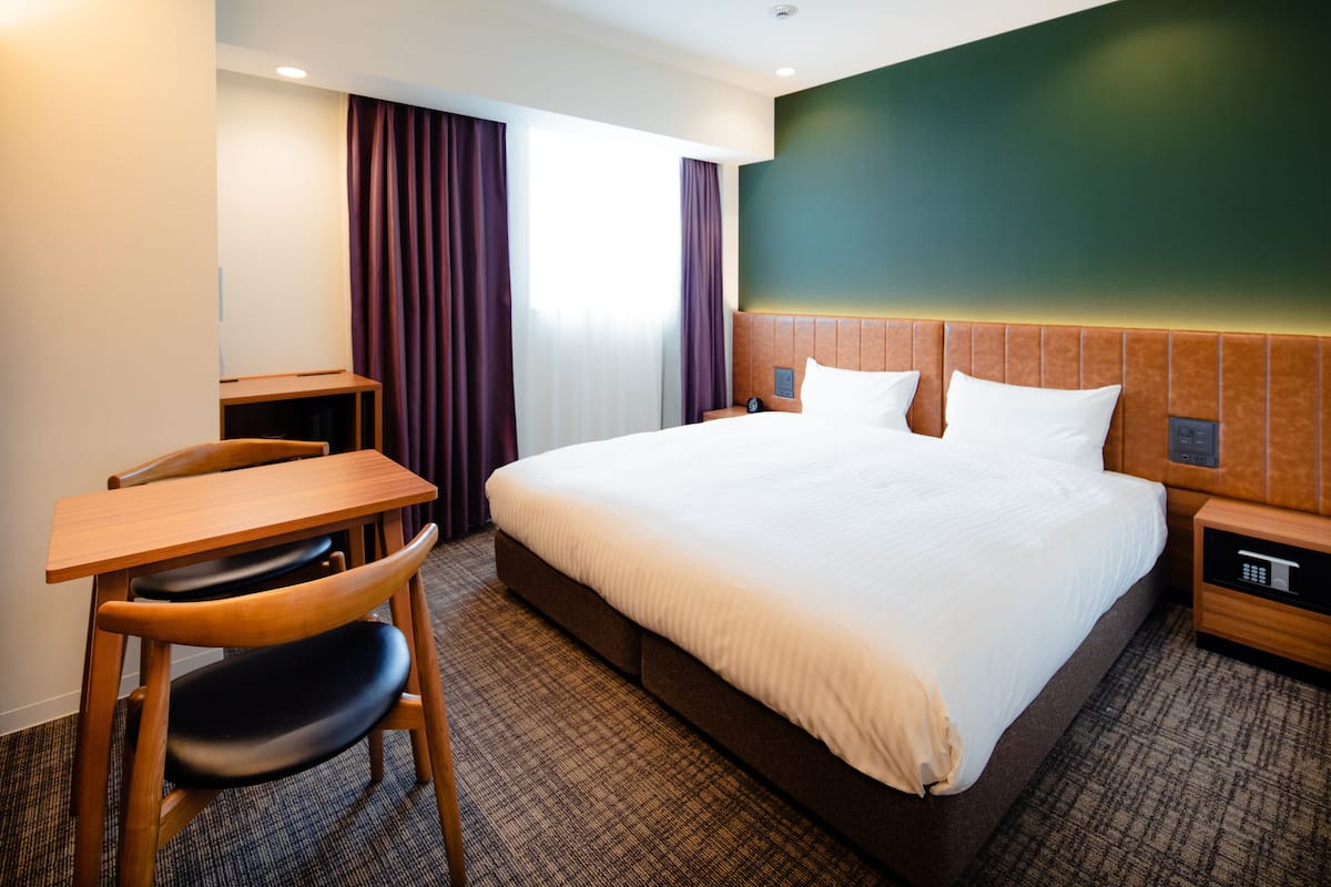 A hotel room with a large bed, a desk, and a chair.
