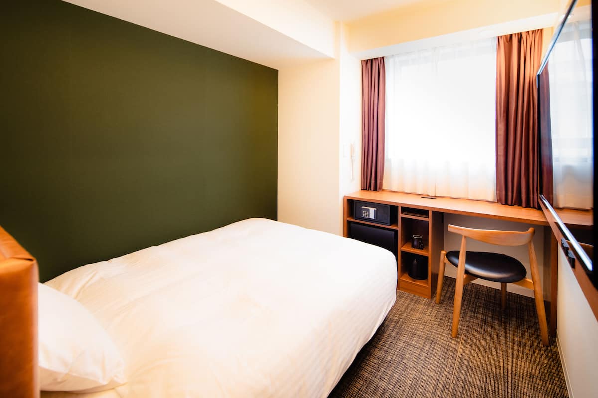 A hotel room with a bed, a desk, a chair, and a window with curtains.