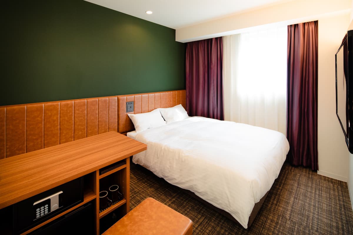 A hotel room with a bed, wooden headboard, a small table, and a TV.