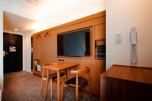 Habitación de hotel con panel de pared de madera, televisor de pantalla plana, mesa de madera con dos sillas, teléfono y puerta con un letrero.