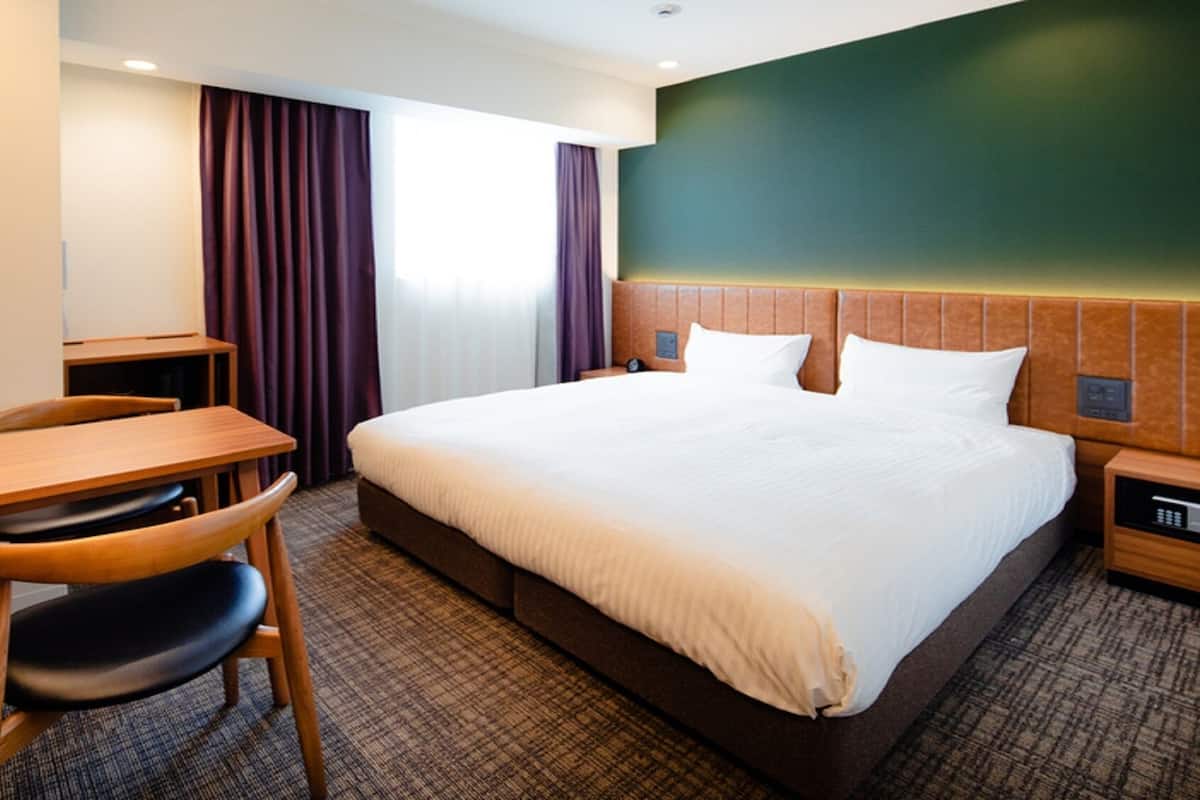 A hotel room with a bed, a desk, a chair, a nightstand, and a wall with a textured pattern.