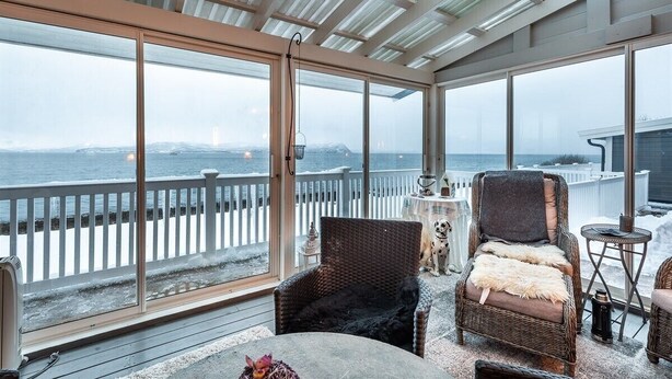 Een overdekt buitengebied met rieten meubels, uitzicht op zee en een witte omheining.