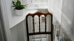 A narrow room with a wooden chair and a potted plant on a window sill. - Hospedaje Menendez Pelayo (Santander)
