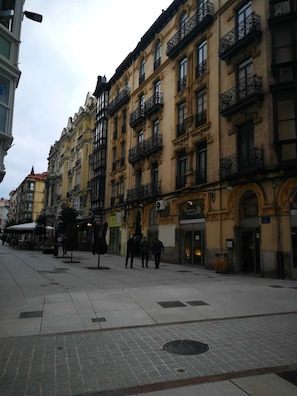 A street with historic buildings, a sidewalk, and a few pedestrians.