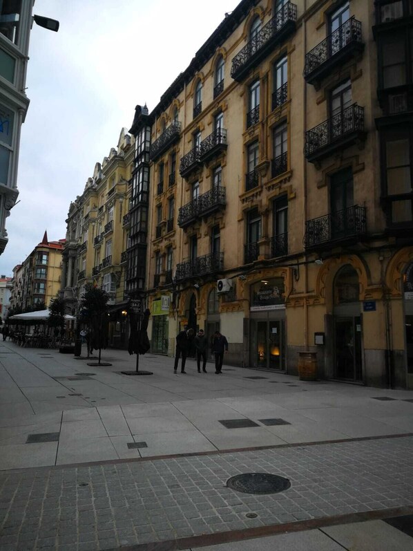 Une rue bordée de bâtiments historiques, un trottoir et quelques piétons.