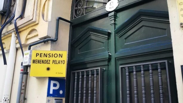 A building entrance with a green door, a yellow sign reading "PENSION MENENDEZ PELAYO", and a blue parking sign. - Hospedaje Menendez Pelayo (Santander)