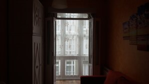 A narrow hallway with a door leading to a balcony with white shutters and a view of buildings. - Hospedaje Menendez Pelayo (Santander)