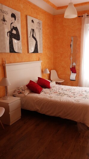 A bedroom with a bed, two nightstands, a lamp, a chair, and two wall art pieces.