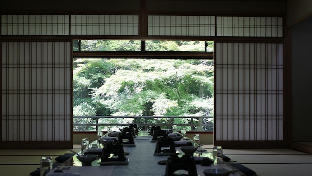 Habitació japonesa tradicional amb sòls de tatami, una taula baixa amb els utensilis per a la cerimònia del te i vista a un jardí exuberant a través de panells shoji.